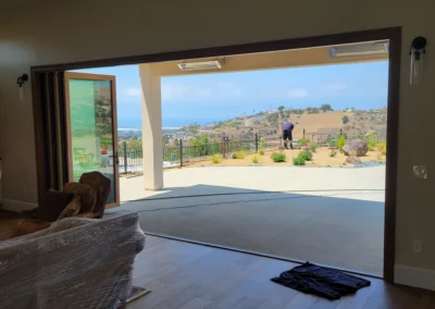 Open sliding doors reveal a scenic outdoor view, with a person tending to the garden on a sunny day. Cozy living room in foreground.