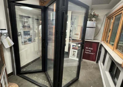 A modern glass door display in a showroom, featuring black frames, with a "Watch Your Step" sign on the floor.