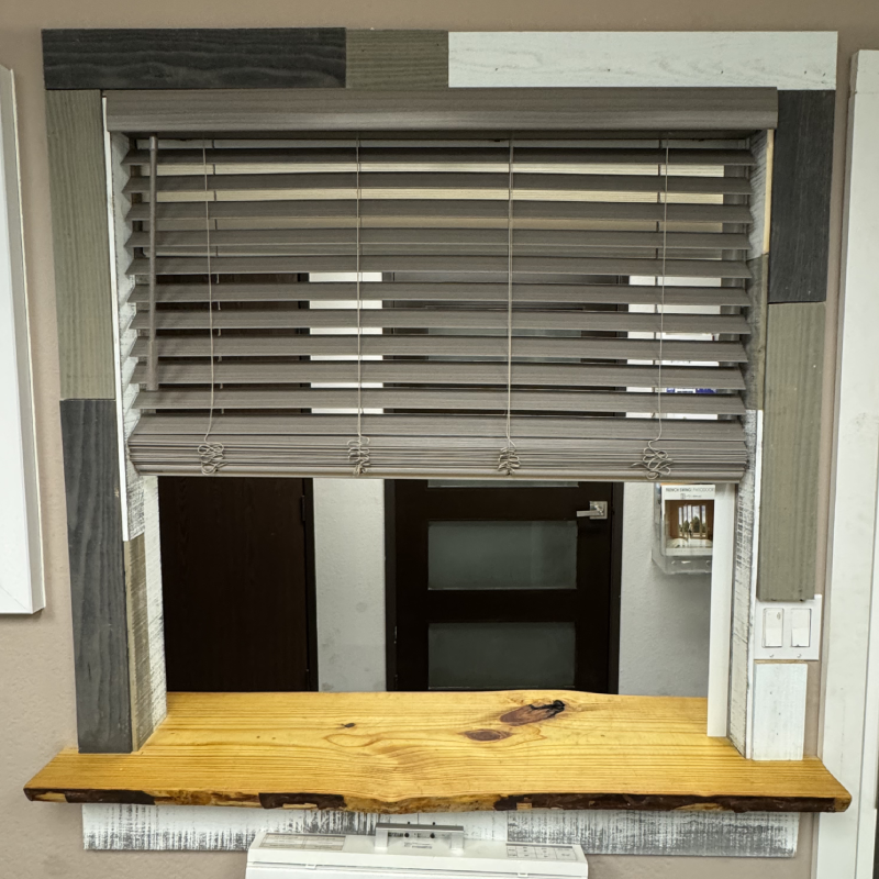 A wooden-framed window with horizontal blinds, featuring a variety of textured wood accents in muted colors and a wooden sill below.